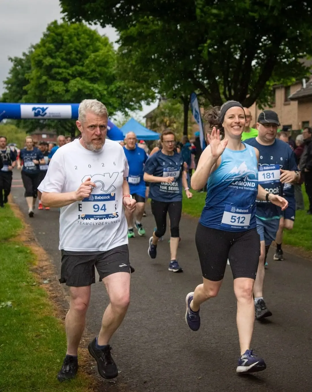 A Lomond runner waving during a busy road race
