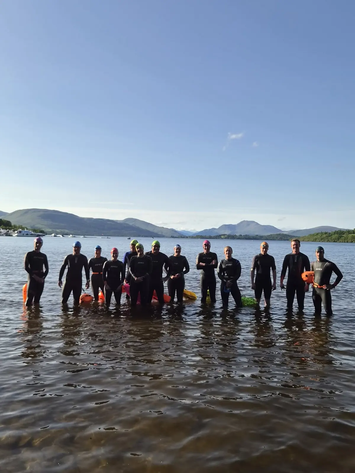 A group of Lomond swimmers standing in Loch Lomond on a sunny evening